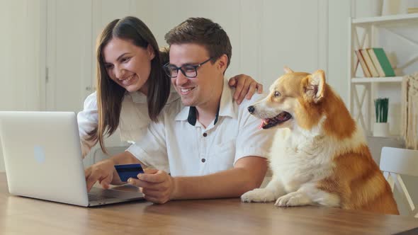 Cheerful Young Couple With a Dog Shopping Online While Sitting Home. Mutual Family's Purchases.