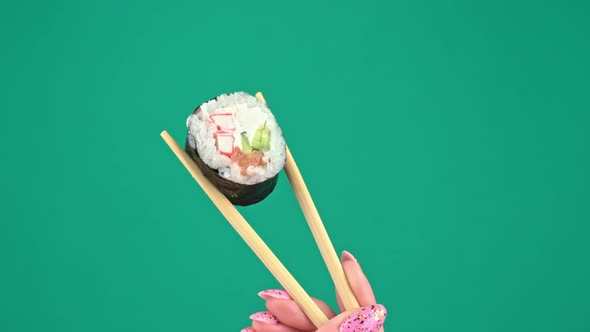 Female Hands Hold Japanese Chopsticks with Sushi Rolls on Green Background