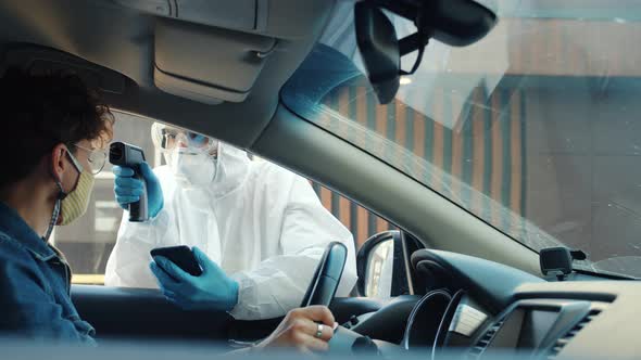 Specialist in Medical Suit Testing Car Driver Taking Body Temperature Talking Outdoors in City