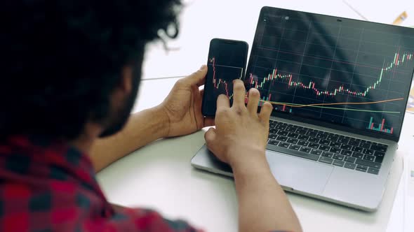 Smart Man Investor and Crypto Trader Using Laptop and Cellphone Analyzes Charts of Trading in Stock