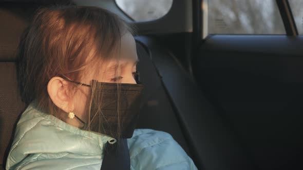 A Child Girl in Car Putting on Black Protective Face Mask As a Protection Against Virus Disease