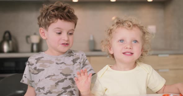 Adorable Brother and Sister Smile and Laugh Together While Sitting at the Kitchen Table Boy Puts His