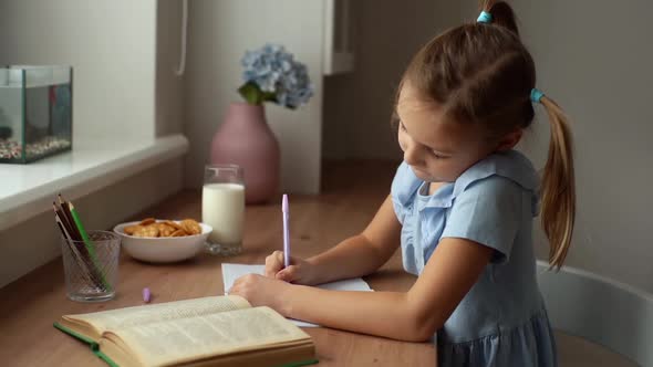 Side View of Thinking Child Schoolgirl Learning at Home Sitting at Table with Cookies and Milk By