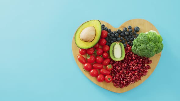 Video of fresh fruit and vegetables with copy space on heart shaped wooden board on blue background