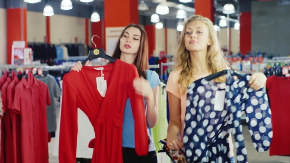 Young Woman Looking at the Summer Dresses In a Store. They Stand in Front of Mirror