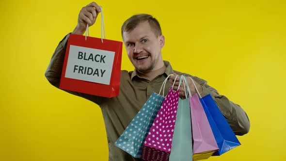 Man Showing Black Friday Inscription on Shopping Bags, Smiling, Satisfied with Low Prices Purchases