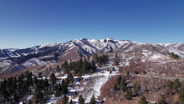 Drone shot pushing forward revealing a snow covered mountain with trees