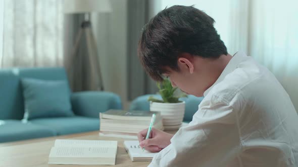 Asian Man Student Writing In Notebook On The Table While Studying At Home