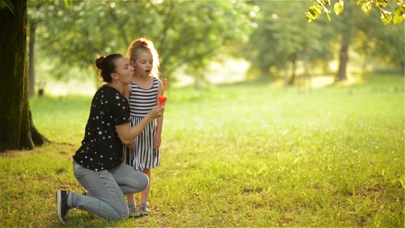 Beautiful Mother With Her Daughter in Nature Making Soap Bubbles and Laughing