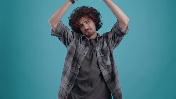 Young Hipster Safely with His Hands Above His Head Emits a Roof with Curly Hair in the Studio on a