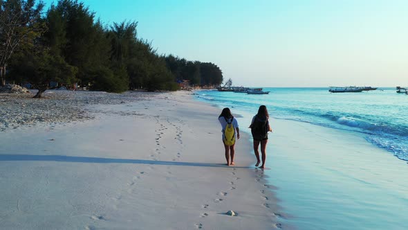 Beautiful happy ladies on photoshoot by the sea at the beach on summer white sand and blue backgroun