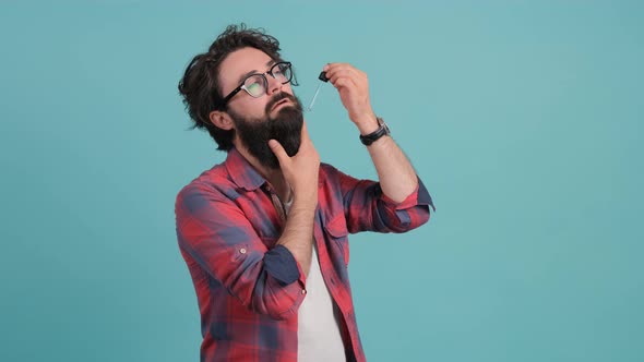 Bearded Man Applies His Beard Care Oil, Isolated on a Turquoise Background