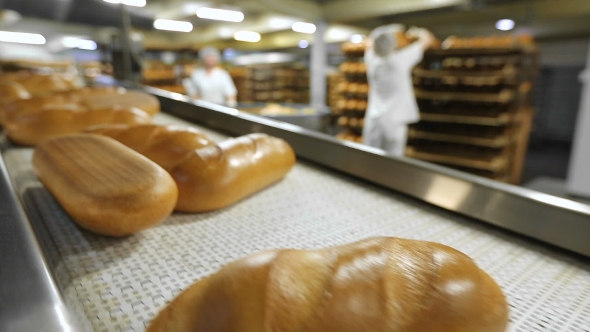 Bread On The Conveyor In The Background Of The Workers In The Bakery