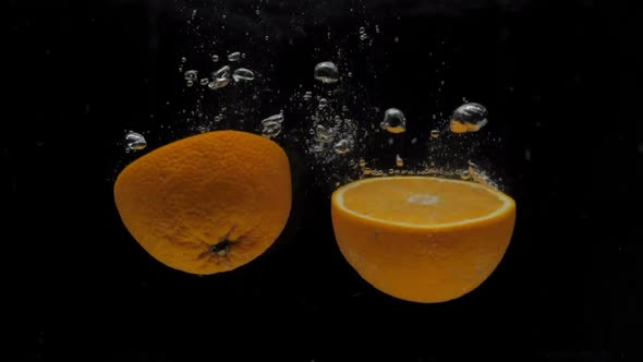 Slow Motion Orange Halves Falling Into Transparent Water on Black Background