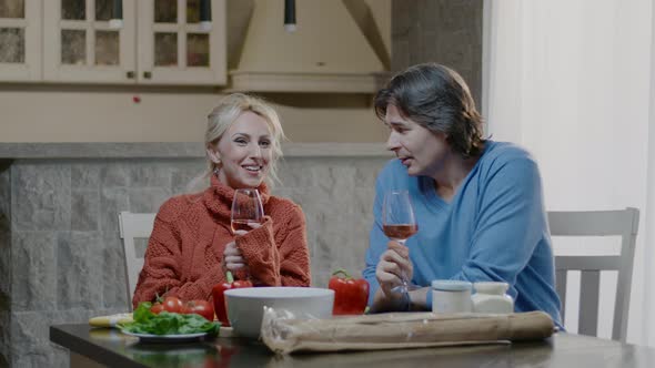 Smiling blonde woman and  man talk with a glass of wine have dinner in the kitchen at home.