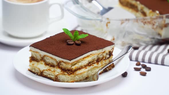 Traditional Italian Tiramisu dessert in glass baking dish, portion on plate and cup of coffee