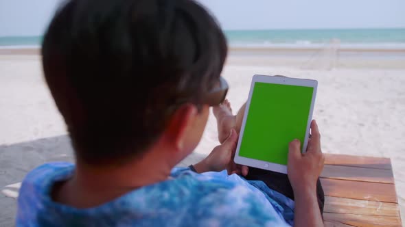 Asian woman watching something on her tablet while relaxing on the beach.
