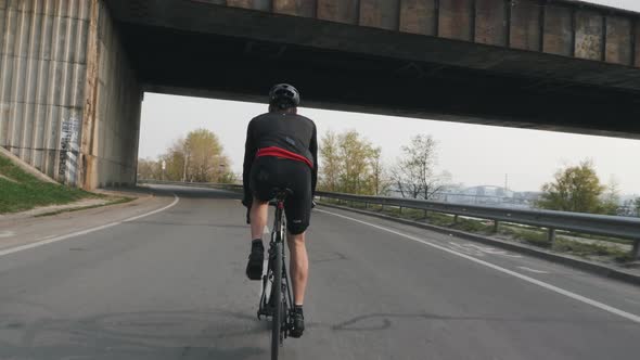 Fit athletic cyclist riding bicycle under the bridge training