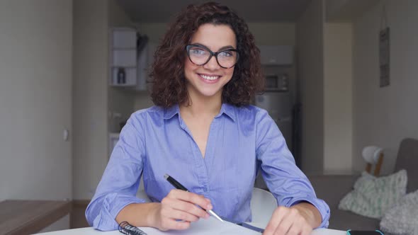 Happy Hispanic Young Female Student Studying at Home and Looking at Camera