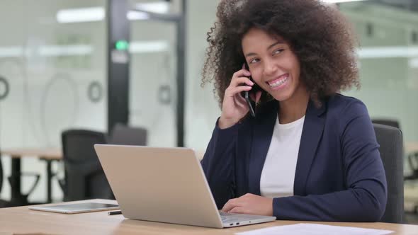 Young African Businesswoman with Laptop Talking on Smartphone