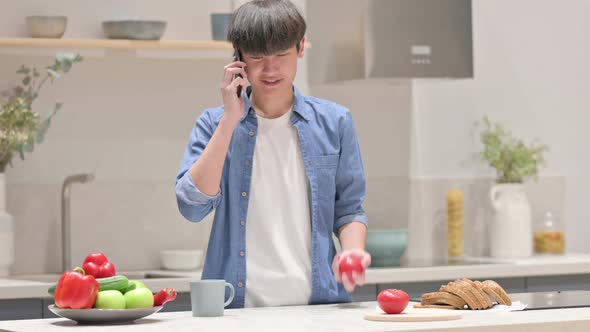 Young Asian Man Talking on Smartphone While Standing in Kitchen