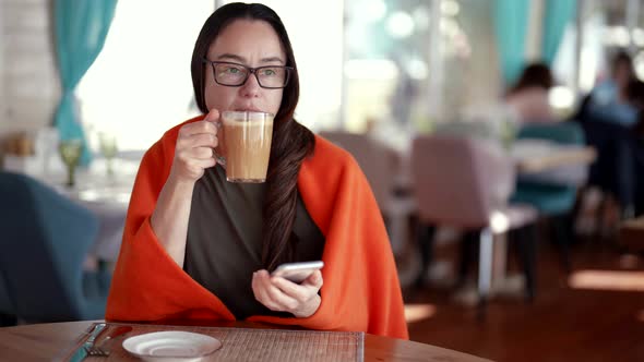 Brunette Woman is Drinking Coffee Restaurant Viewing Video or Pictures in Smartphone