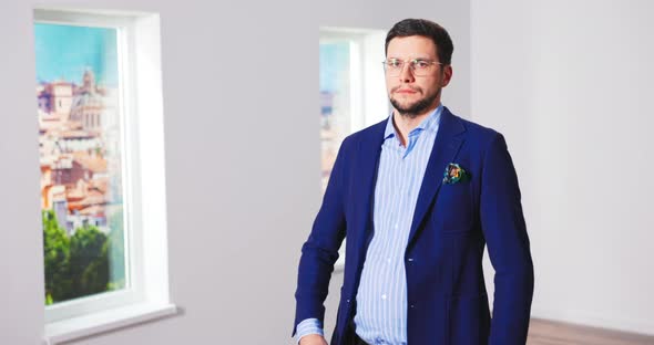 Portrait of Handsome Young Caucasian Male Real Estate Agent in Suit Standing in Empty Apartment