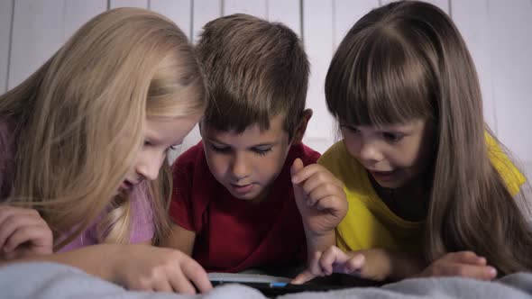 Children Learn Modern Technology, Little Friends in Multicolor T-shirts Use Tablet Computer Lying on
