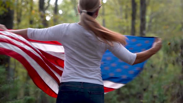 Pretty blonde woman with sunglasses on in a forest spinning around to the left with a US flag flying