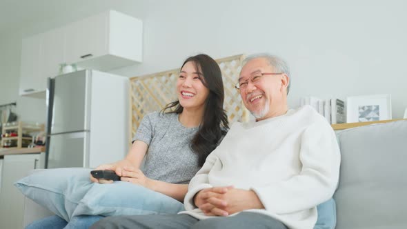 Asian senior father and daughter watch funny movie together at home.