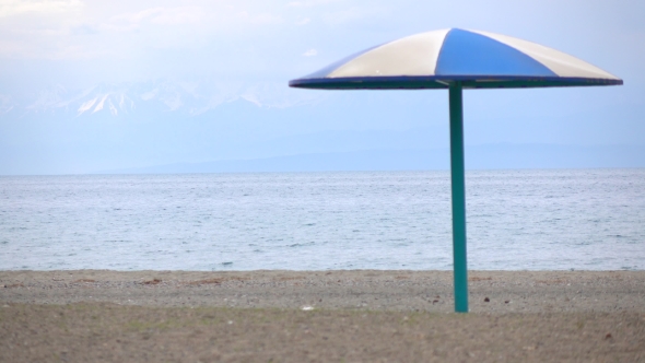 Empty Beach And Blue Sun Umbrella Against Snow Peaks