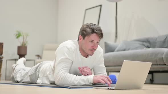 Middle Aged Man Using Laptop on Yoga Mat at Home