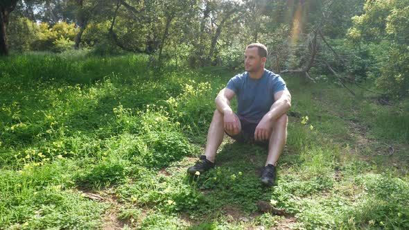 A handsome man sitting into a meditation pose in a green grassy forest meadow in nature on a bright