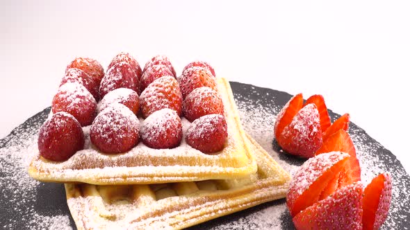 Belgian waffles with strawberry and powdered sugar on a stone board on a white background.