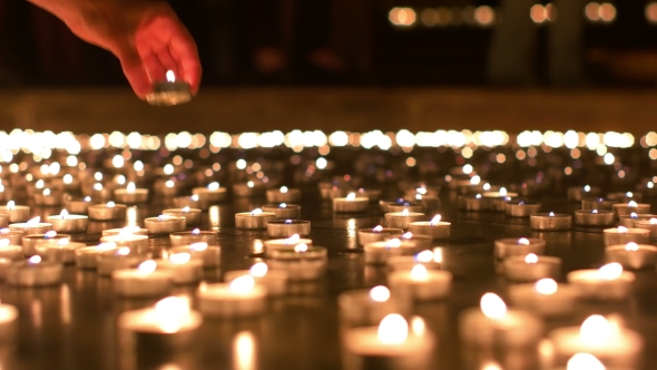 Woman Placing Her Candle In Between Other Candles alt