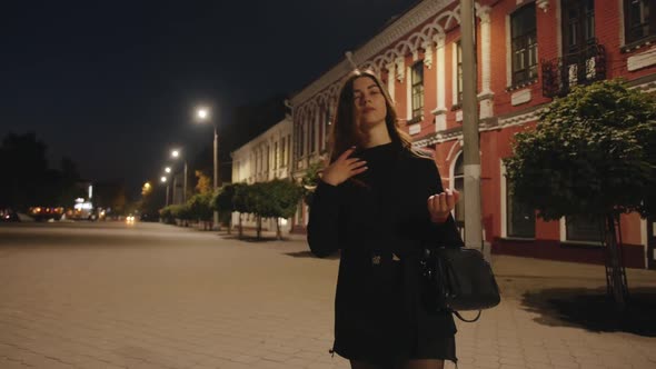 An Elegant Young Girl Walks Along the Illuminated Pedestrian Zone of the Evening City and Enjoys a