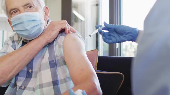 Video of hands of biracial female doctor vaccinating caucasian senior man