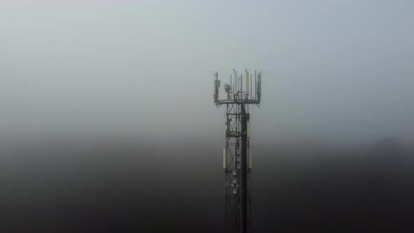 Aerial backwards flight showing top of cellular antenna tower disappear in mist