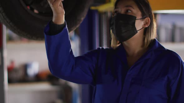 Female mechanic wearing face mask holding digital tablet inspecting the car at a car service station