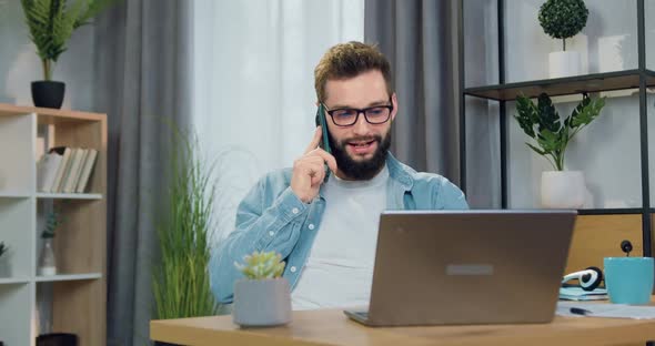 Male Worker in Glasses which Sitting in Front of Computer at Home and Talking on mobile