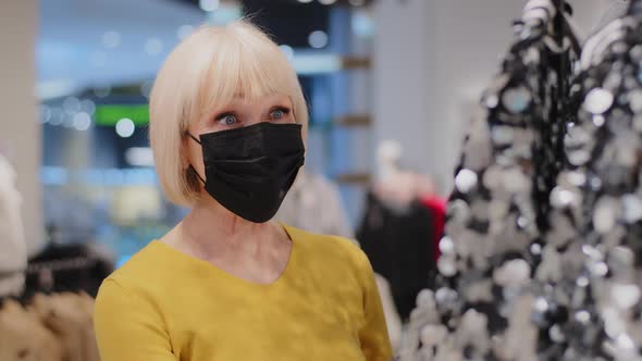 Mature Woman Shopper in Protective Mask in Clothing Store Admires Shiny Outfit Elderly Lady Looks