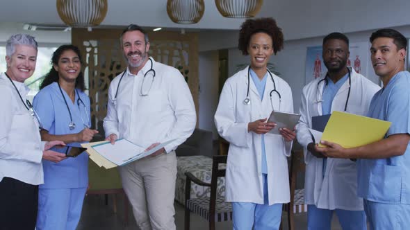 Portrait of diverse male and female doctors standing in hospital corridor smiling to camera