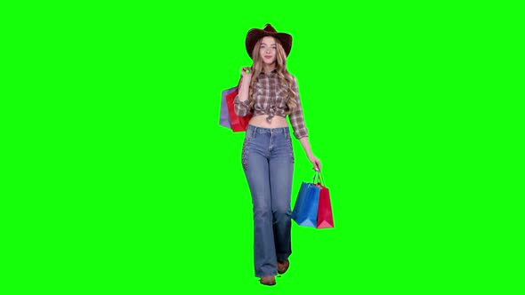 Girl in a Hat and Cowboy Boots Comes with Bags in Her Hands. Green Screen
