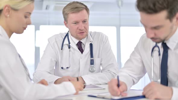 Young Male Doctor Writing on Paper and Listening To Senior Doctor