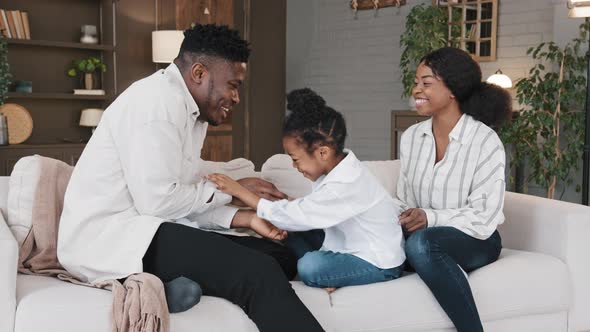 Happy African Family Mum Dad with Cute Little Kid Daughter Tickling Having Fun Relax on Sofa