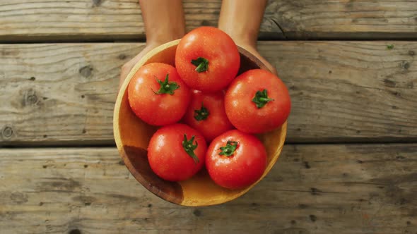 Video of biracial man holding bowl of fresh red tomatoes on wooden background