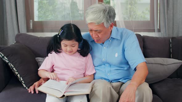 Senior Chinese, grandpa happy relax with young granddaughter girl enjoy read books and do homework.