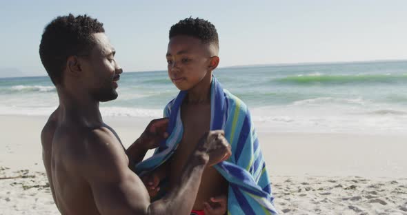 Smiling african american father toweling off his son on sunny beach