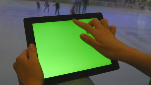 Female Hands Using Tablet Pc With Green Screen In Shopping Mall. Lot Of People Skate On Indoor Ice