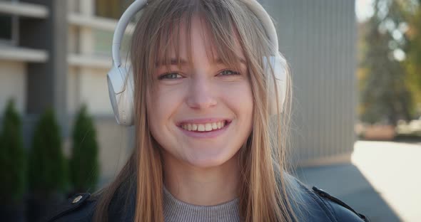 Smilling Female Student in Headphone Listen Music and Looking in Camera Standing in Outdoor